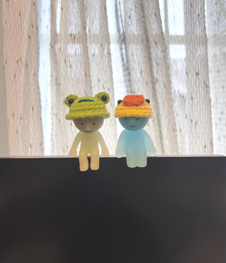 two small toy animals sitting on top of a black surface next to a window with curtains