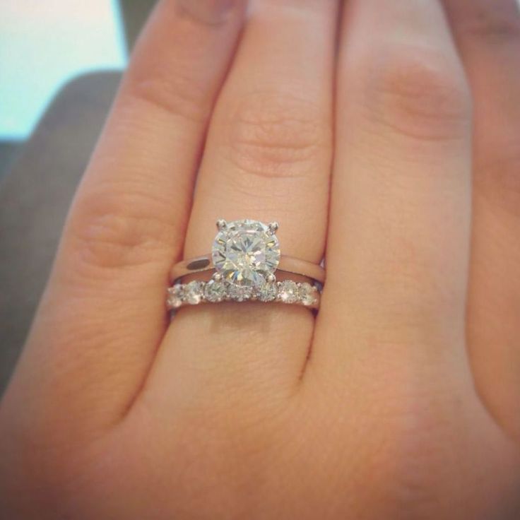 a woman's hand with a diamond ring on top of her finger and the other hand holding an engagement ring