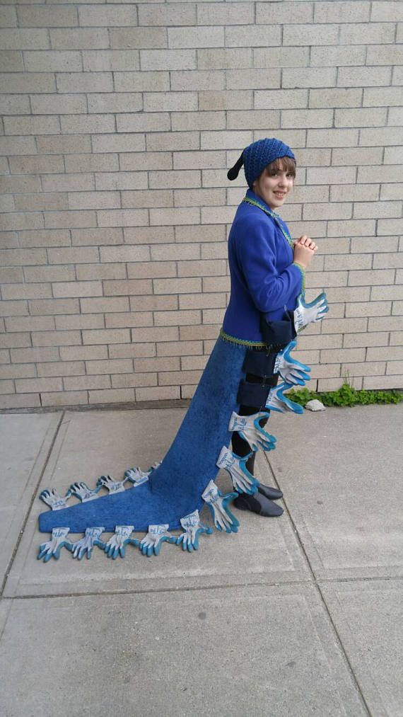 a young boy dressed up as a blue dragon with his hands in the air, standing next to a brick wall