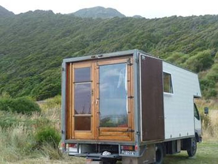 a truck is parked on the side of a hill with a small house in the back