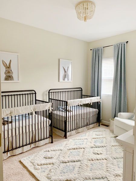 two baby cribs in a nursery with blue drapes