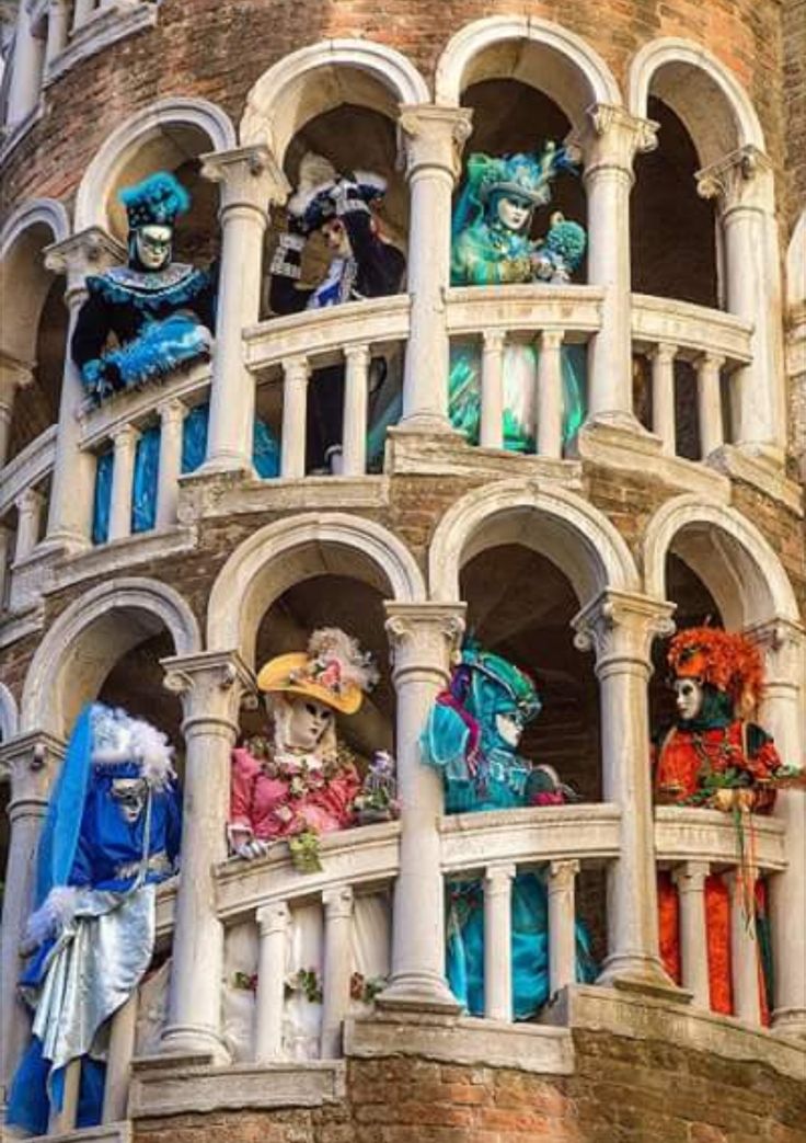 many colorful masks are on display in the windows of an old brick building with arched balconies