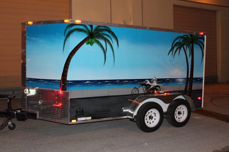 a trailer with a palm tree painted on the side and a motorcycle parked next to it