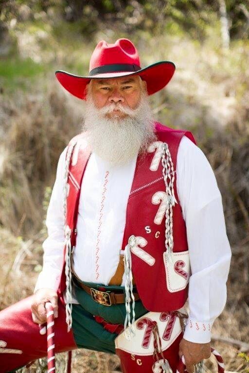 a man with a long white beard wearing a red vest and hat sitting on the ground