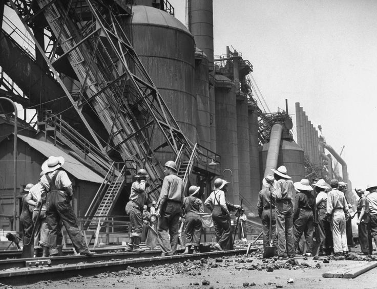 black and white photograph of men working on an industrial plant with workers standing around it