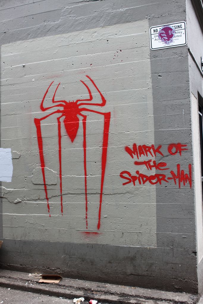 graffiti on the side of a building with red spider - man's head painted on it