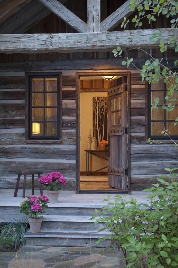 an open door to a cabin with flowers in the foreground and stairs leading up to it