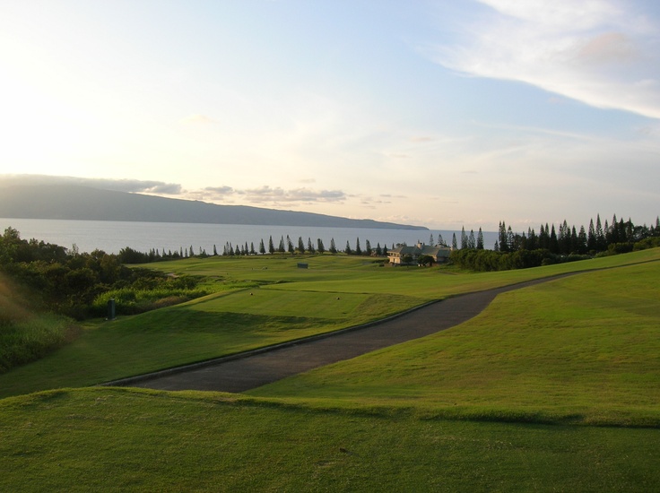 the sun is setting on a golf course by the water and hills in the distance