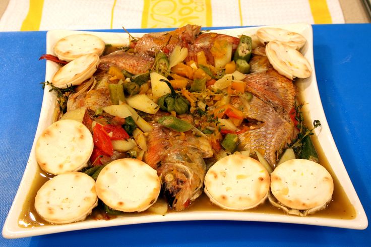 a square plate with fish and vegetables on it sitting on a blue tablecloth covered table