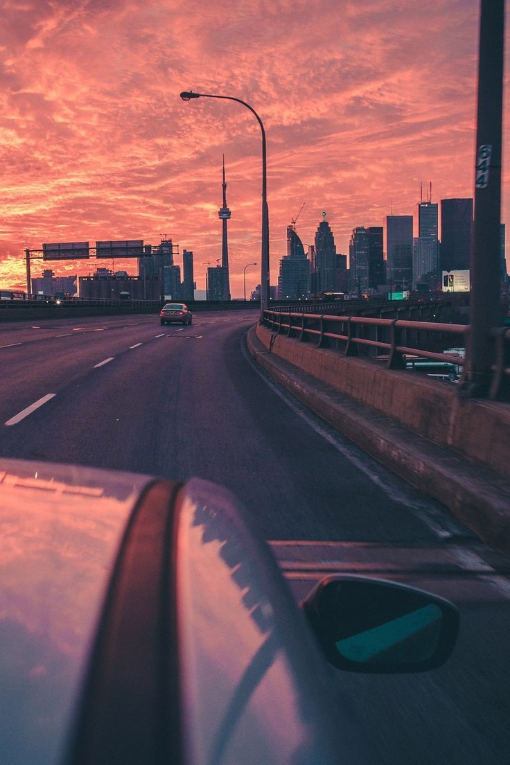 the sun is setting over a city with cars driving down the road in front of it