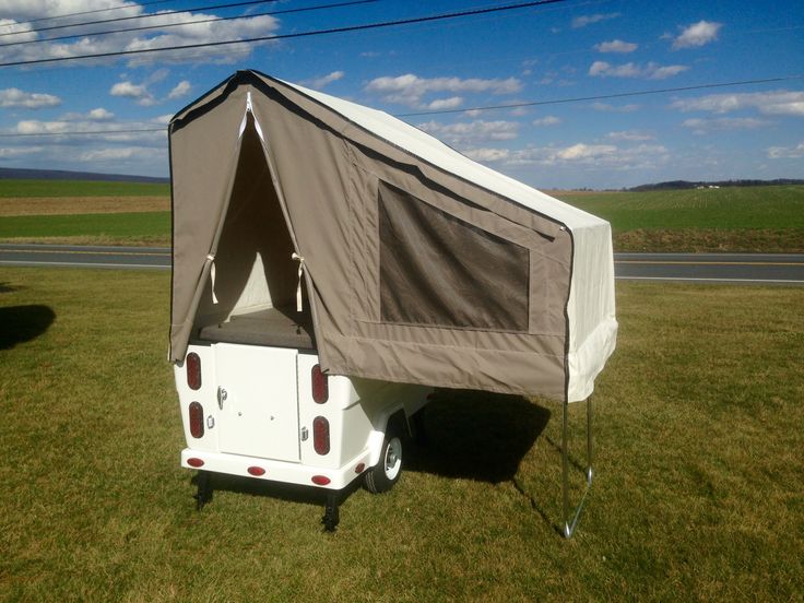 a camper trailer with a tent attached to it's back in the grass