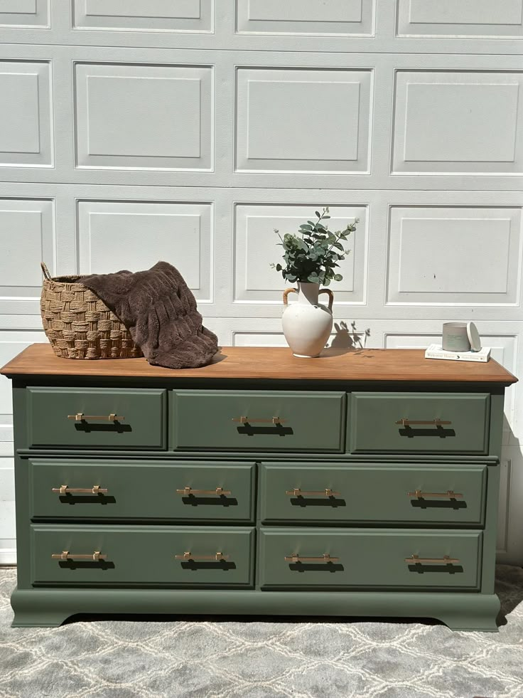 a green dresser with drawers and a potted plant sitting on it's top