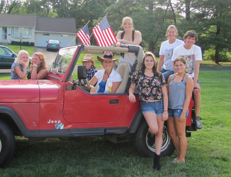 a group of people sitting in the back of a red jeep with an american flag on top