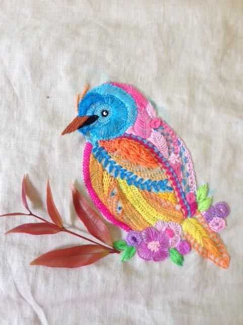 an embroidered bird sitting on top of a white cloth