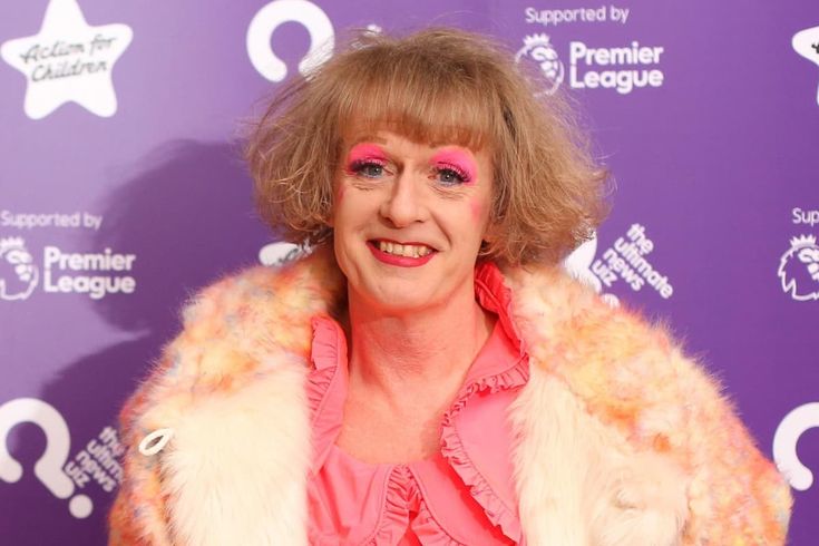 a woman with pink eyeliners and a fur coat smiles at the camera while standing in front of a purple backdrop