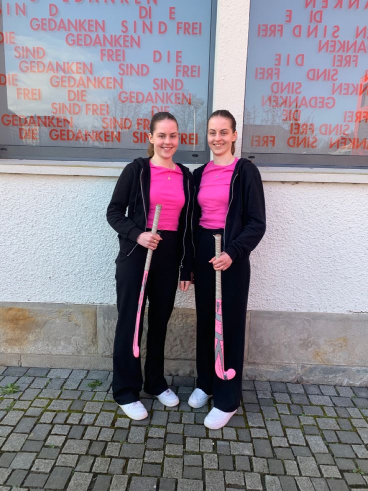 two women standing next to each other in front of a building with pink shirts on