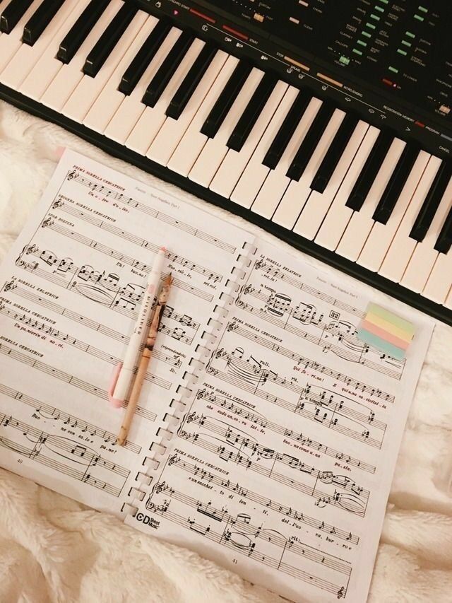 an open sheet of music sitting on top of a white blanket next to a keyboard