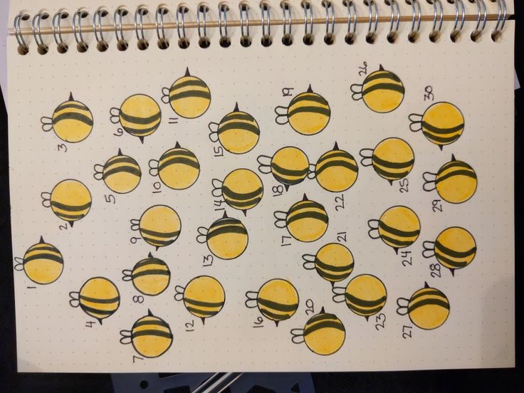 a spiral notebook with yellow and black bee images on the pages, next to a pen