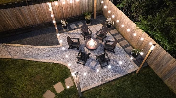 an aerial view of a patio with lights on the ground and chairs around it, in front of a wooden fence