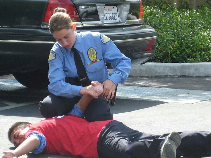 a police officer helping a young boy on the ground in front of a parked car