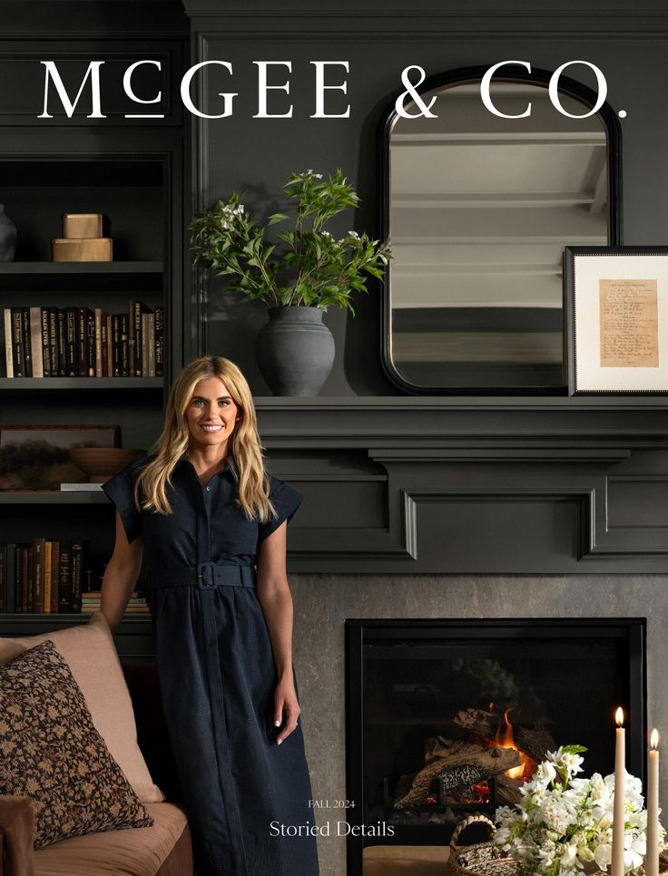 a woman standing in front of a fireplace with candles on the mantel and bookshelves behind her