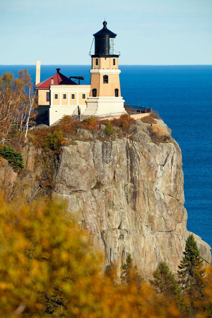 a light house sitting on top of a rocky cliff next to the ocean with trees around it