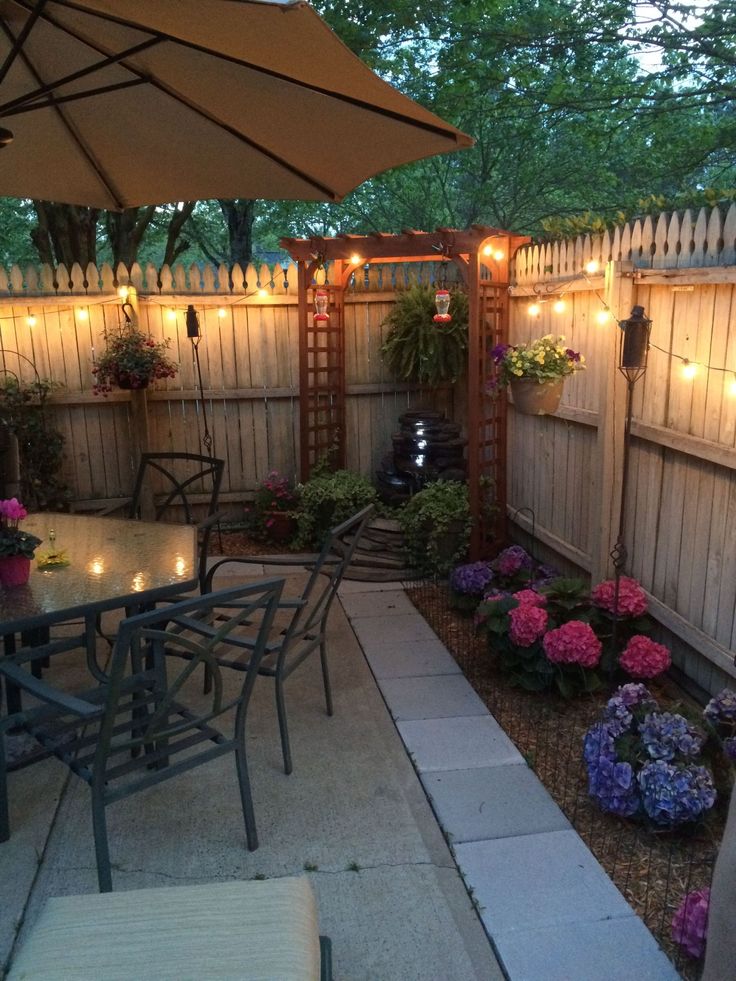 an outdoor dining area with patio furniture and lights on the fence, surrounded by flowers