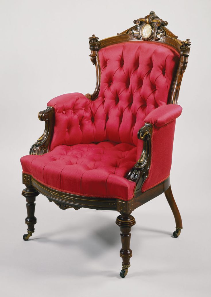 an old fashioned red chair with gold trimmings and buttons on the armrest