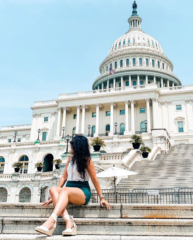 a woman sitting on steps in front of the capitol building with her legs crossed, looking down