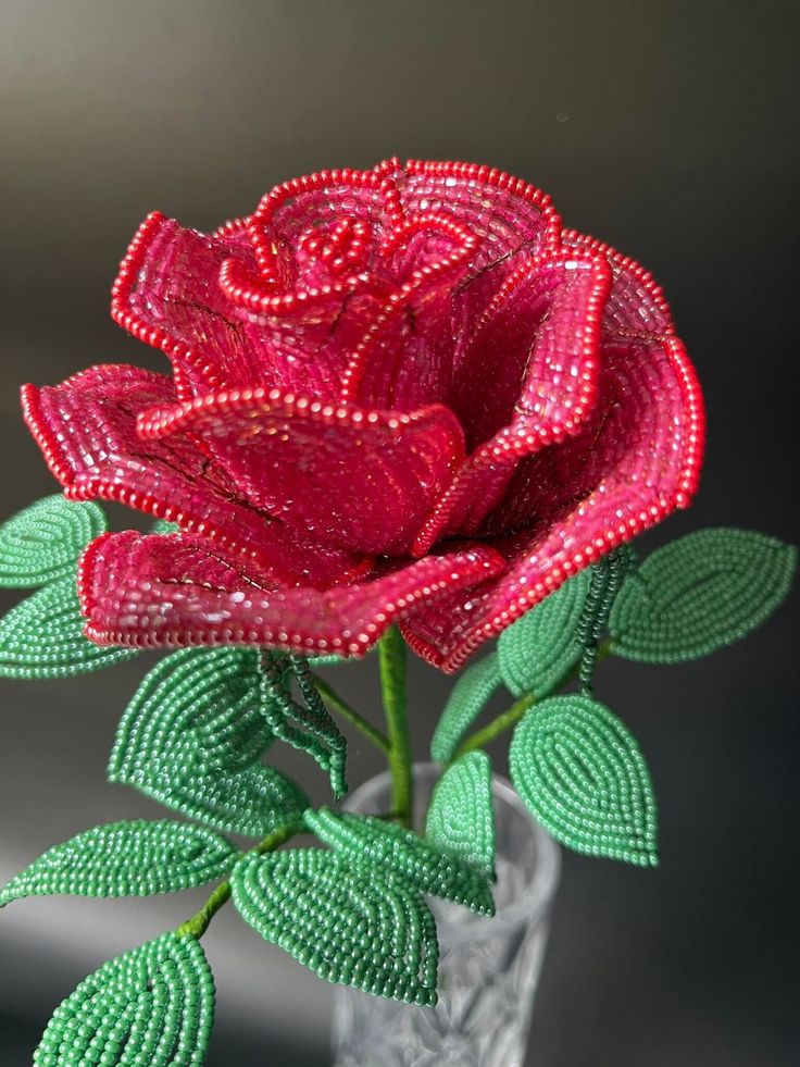 a red rose with green leaves in a glass vase filled with water and beaded beads