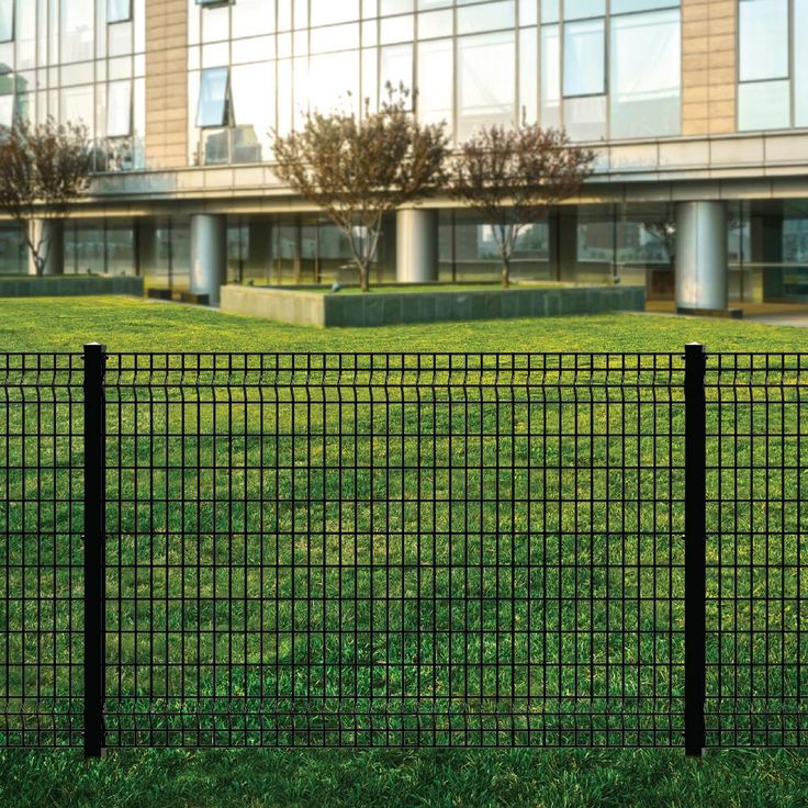 a tall building sitting next to a lush green field in front of a black fence