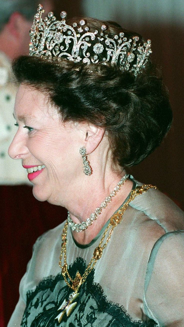 an older woman wearing a tiara and smiling at someone in the background with other people behind her