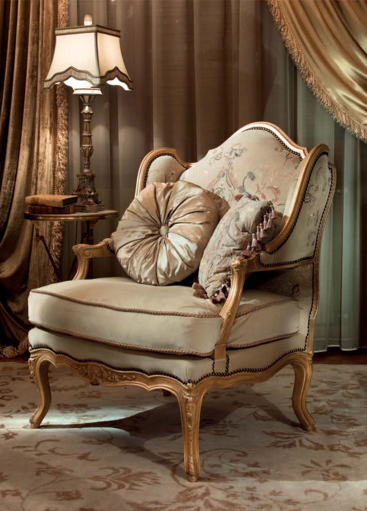 a fancy chair with pillows on it in front of a curtained window and lamp