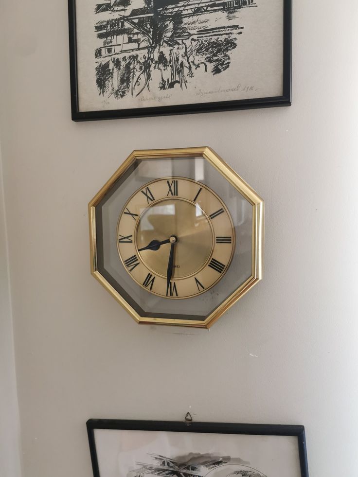 a clock mounted to the side of a wall next to two framed pictures on a wall