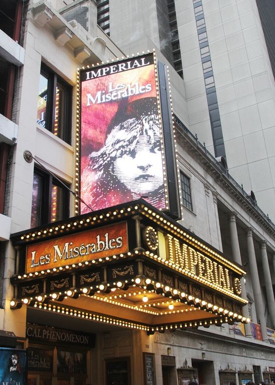 the marquee for les miserables is lit up in front of tall buildings