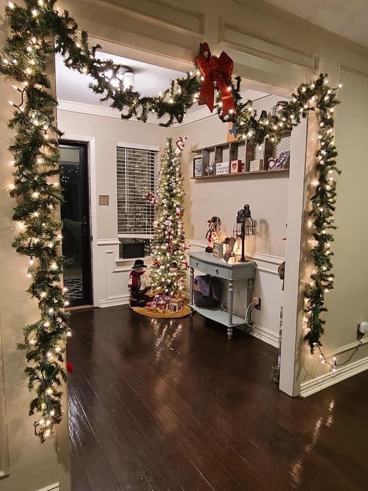 a living room decorated for christmas with lights and garlands on the walls, wood flooring