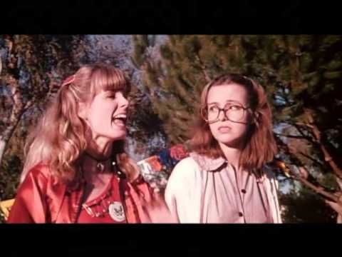 two young women standing next to each other in front of some trees and bushes with their mouths open