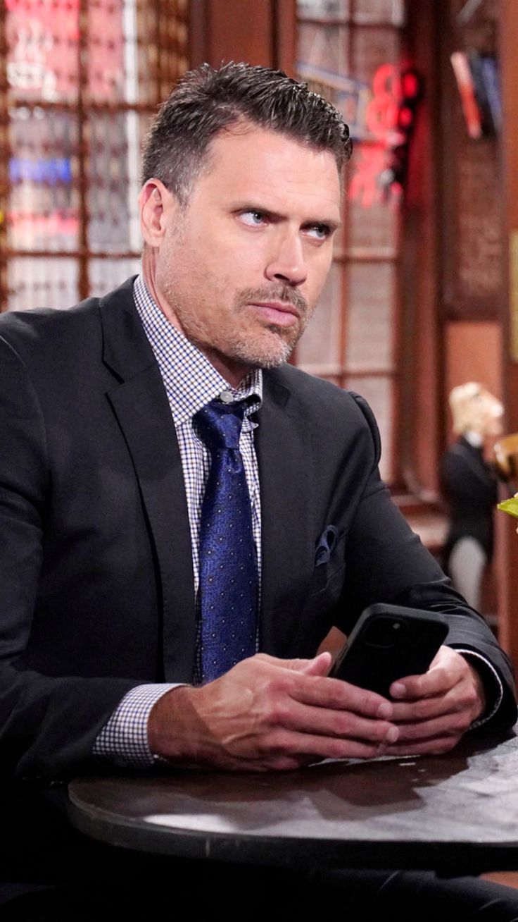 a man in a suit and tie sitting at a table looking at his cell phone