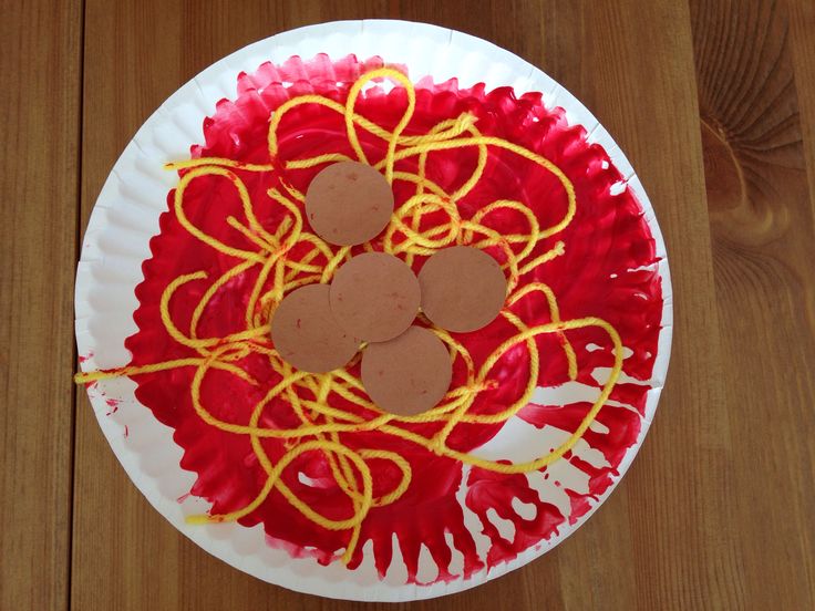 a paper plate topped with spaghetti and mouses on top of a wooden table next to a cupcake