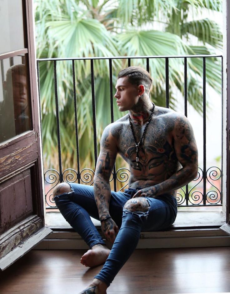 a man with tattoos sitting in front of a window