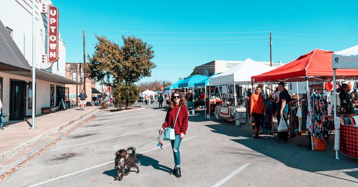 a woman walking her dog down the street at an outdoor market with tents and vendors