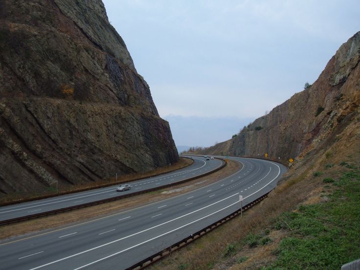 an empty highway is next to a large rock formation on the side of a mountain