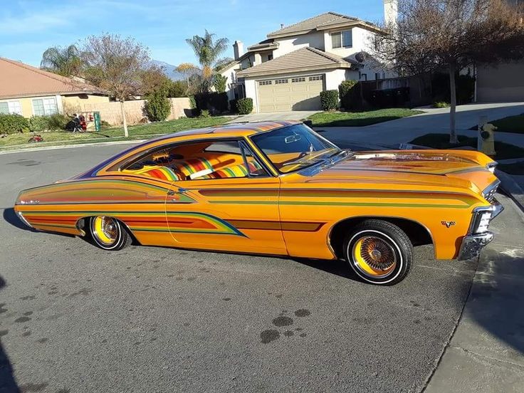 an orange and yellow car parked on the side of a road in front of some houses