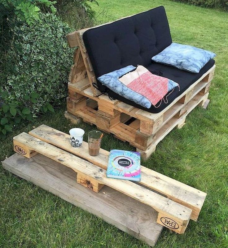 a couch made out of wooden pallets in the grass next to a bench with pillows on it