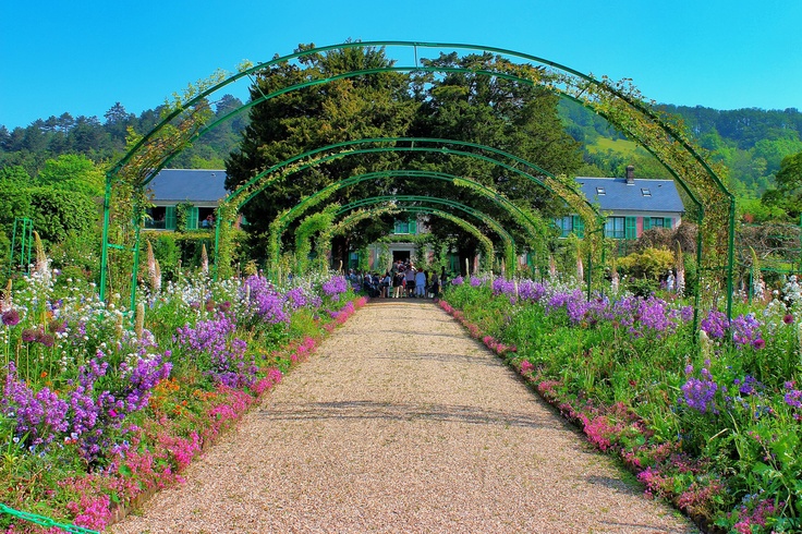 a garden filled with lots of purple and white flowers next to a lush green archway