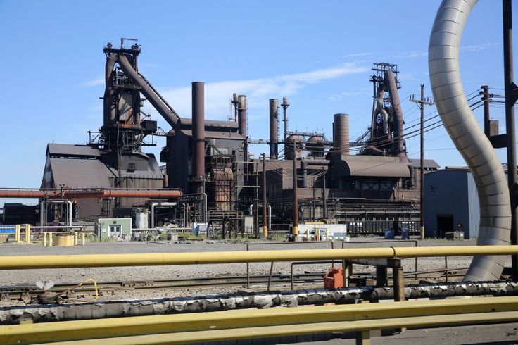 an industrial factory with pipes and machinery in the foreground, against a blue sky