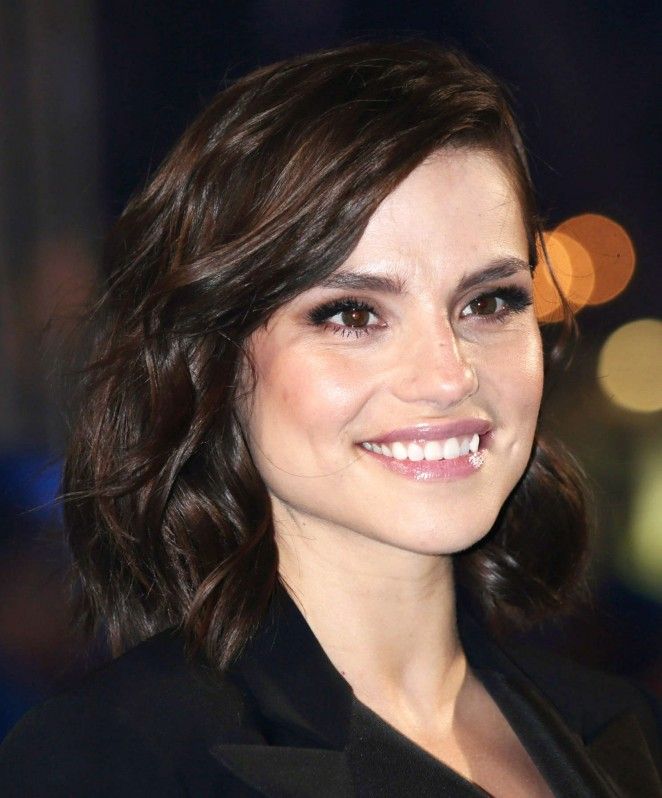 a close up of a person wearing a suit and smiling at the camera with blurry lights in the background