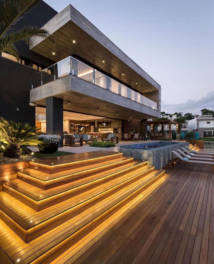 an outdoor deck with steps leading up to a large house that is lit up at night