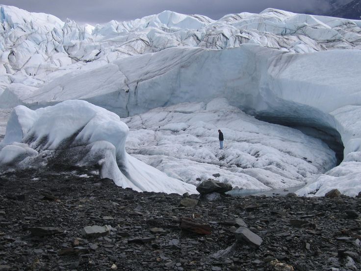 a man standing in front of an ice cave on the side of a snowy mountain