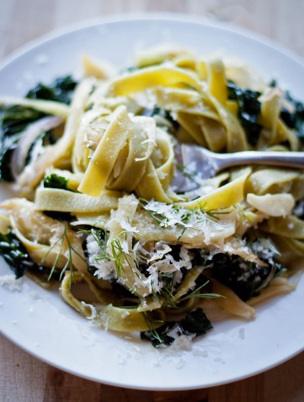 a white plate topped with pasta and spinach covered in parmesan cheese on top of a wooden table